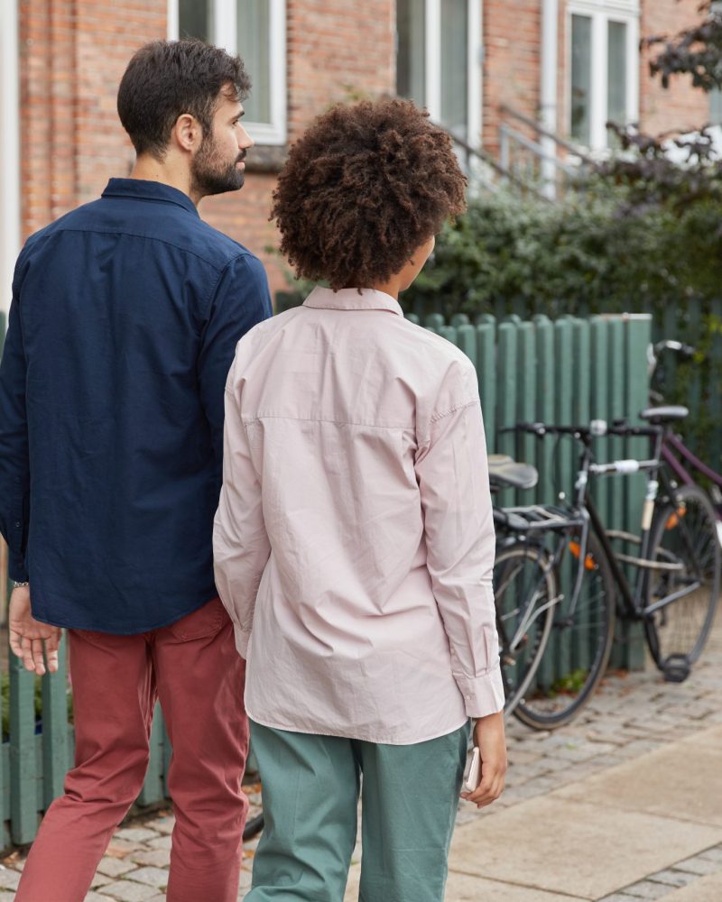 Back view of mixed race couple hold hands, return home after outdoor walk, going to ride bike, wear stylish outfit, have pleasant talk with each other. Relationships, friendship, street style concept
