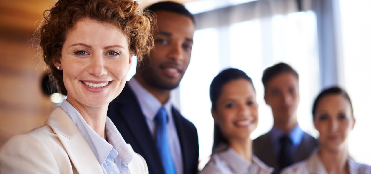 Portrait of an attractive businesswoman with her colleagues standing behind her.