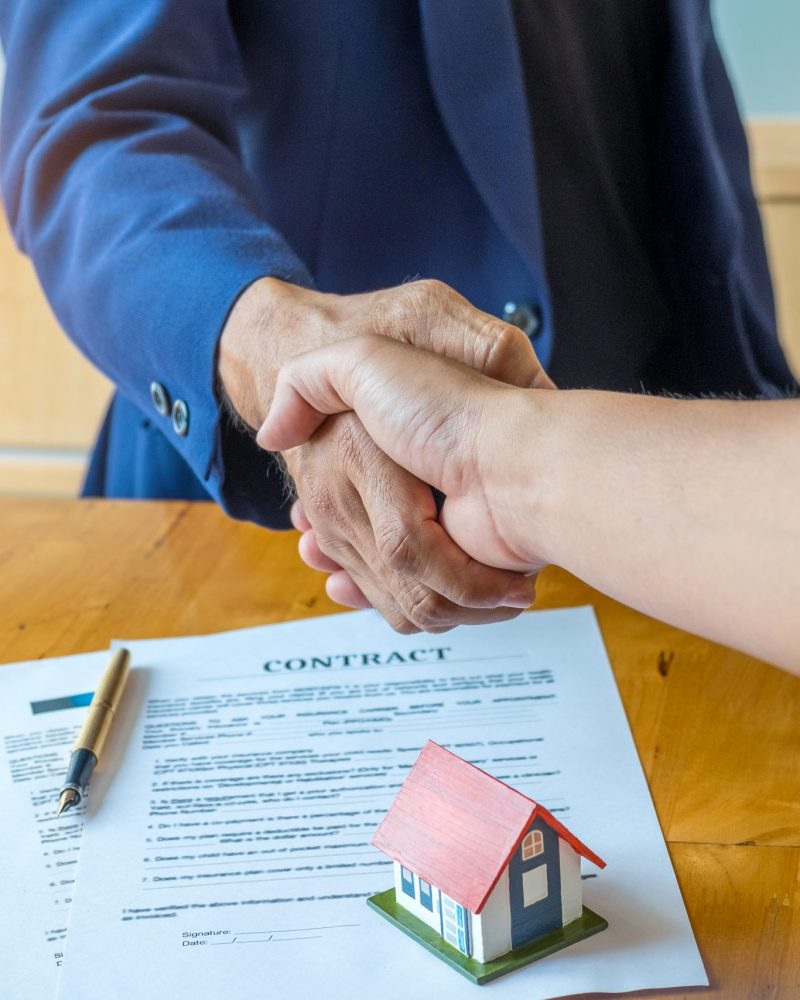 Shake hands for home trading. Between brokers and clients,Model house and contract put on the table,top view shot.
