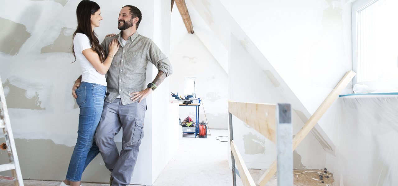 Smiling couple standing in attic to be renovated